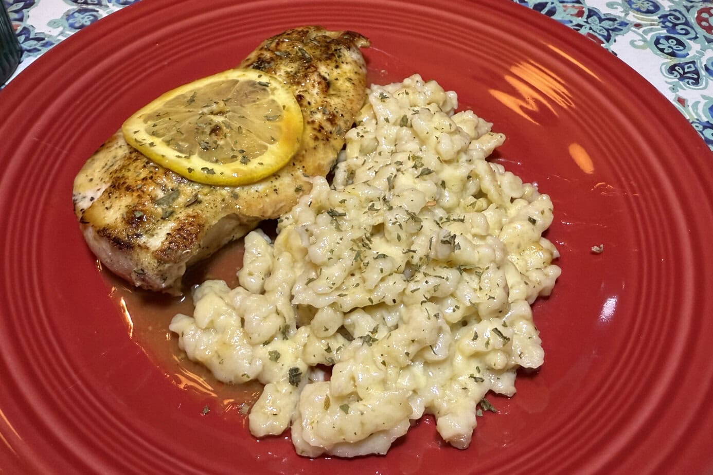 A red plat with German Spätzle dumplings and grilled chicken.