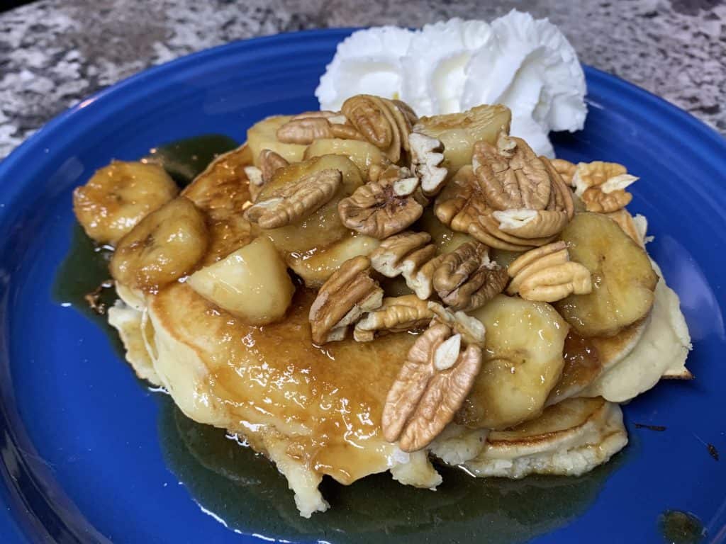 Pancakes on a blue plate topped with Bananas Foster and whipped cream