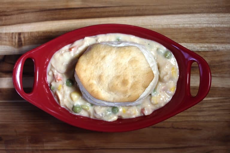 overhead view of red bowl filled with chicken pot pie filling sitting on top of wooden tray