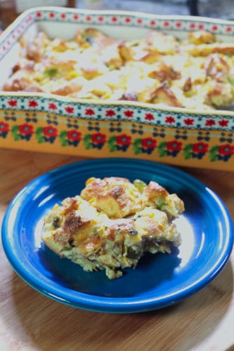 Serving of savory bread pudding on a blue plate with a baking dish in the background